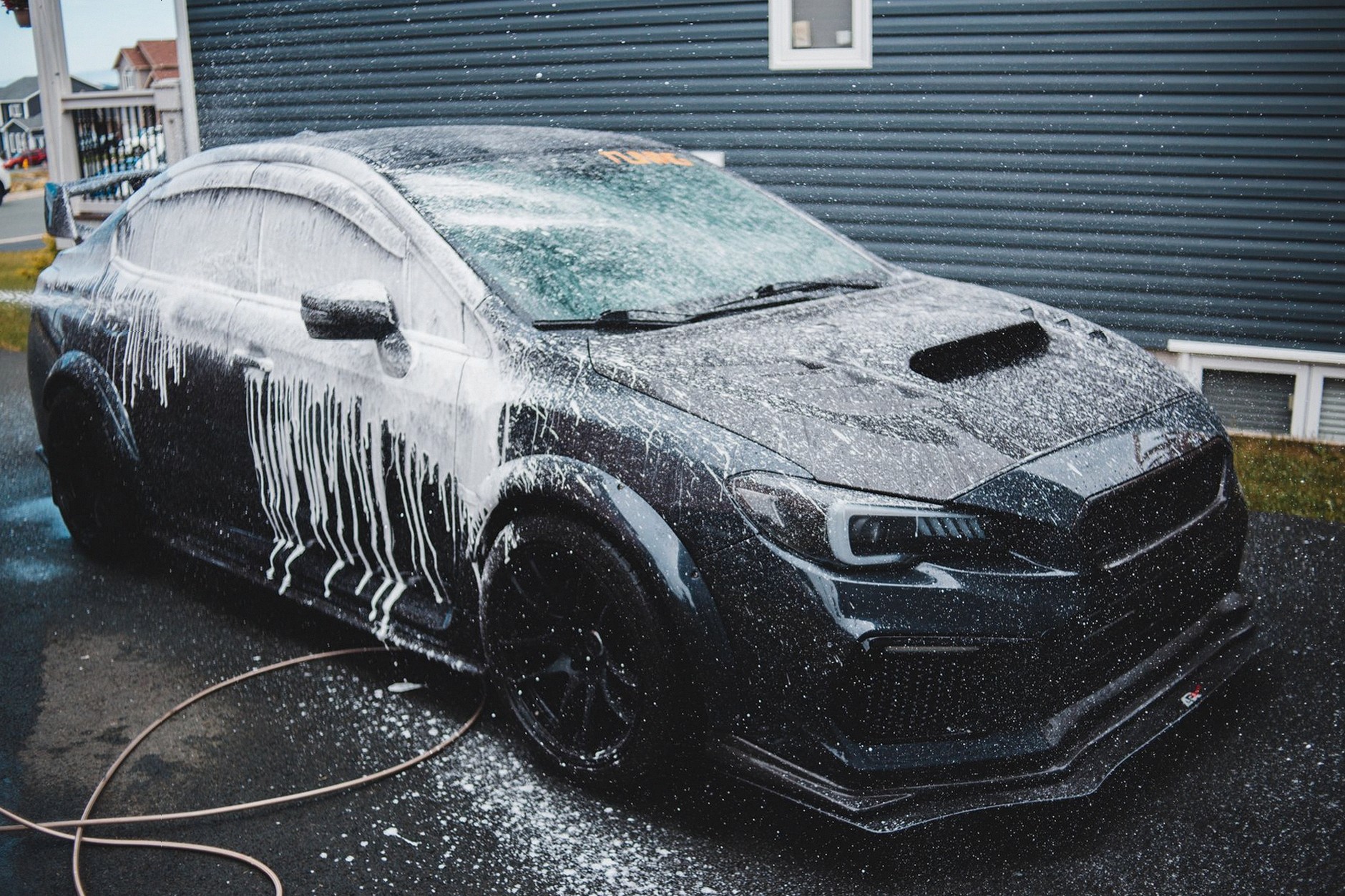Black expensive tuned sports car under car wash next to cottage in daytime