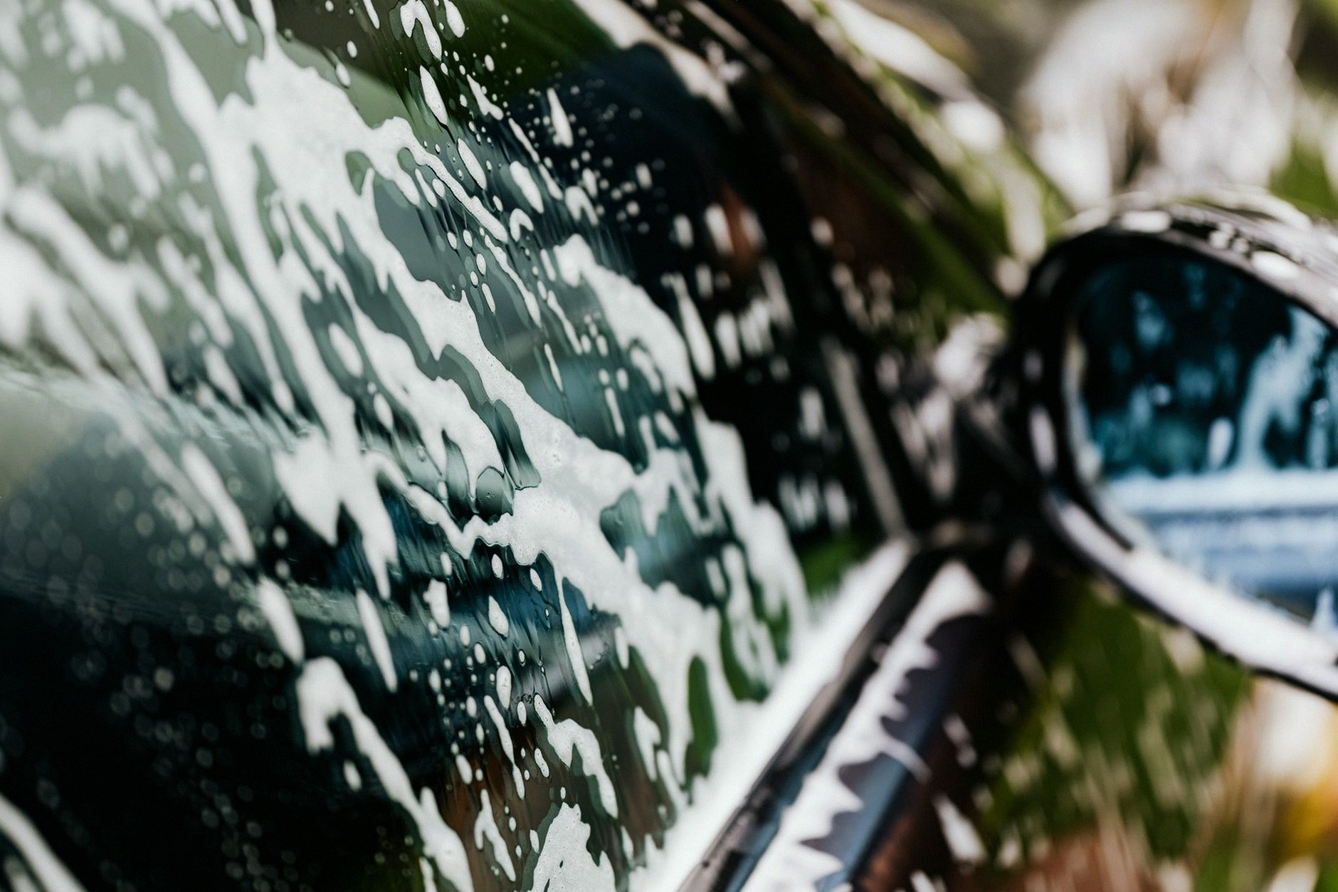 Detailed view of car covered in soapy foam during a wash, highlighting cleanliness.
