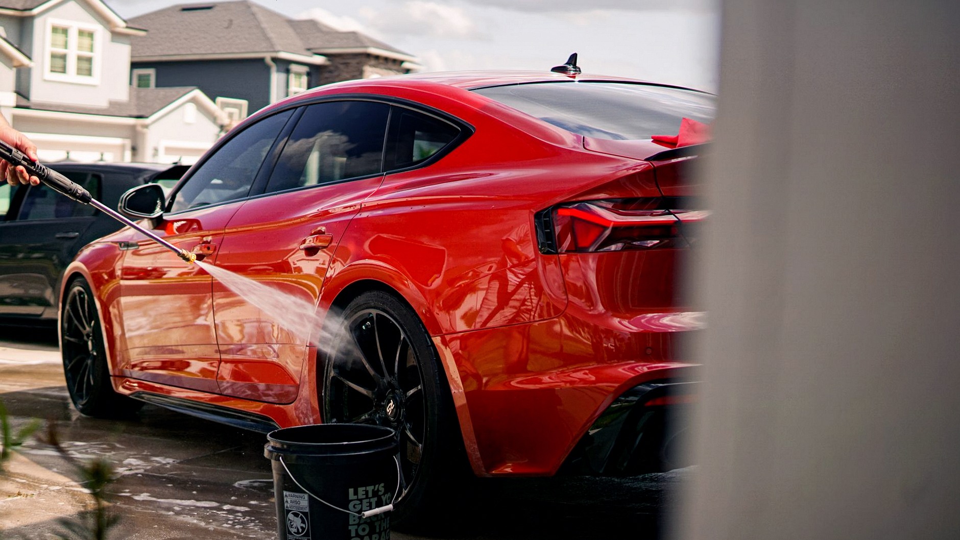 A vibrant red luxury car being washed outdoors in a suburban residential area.