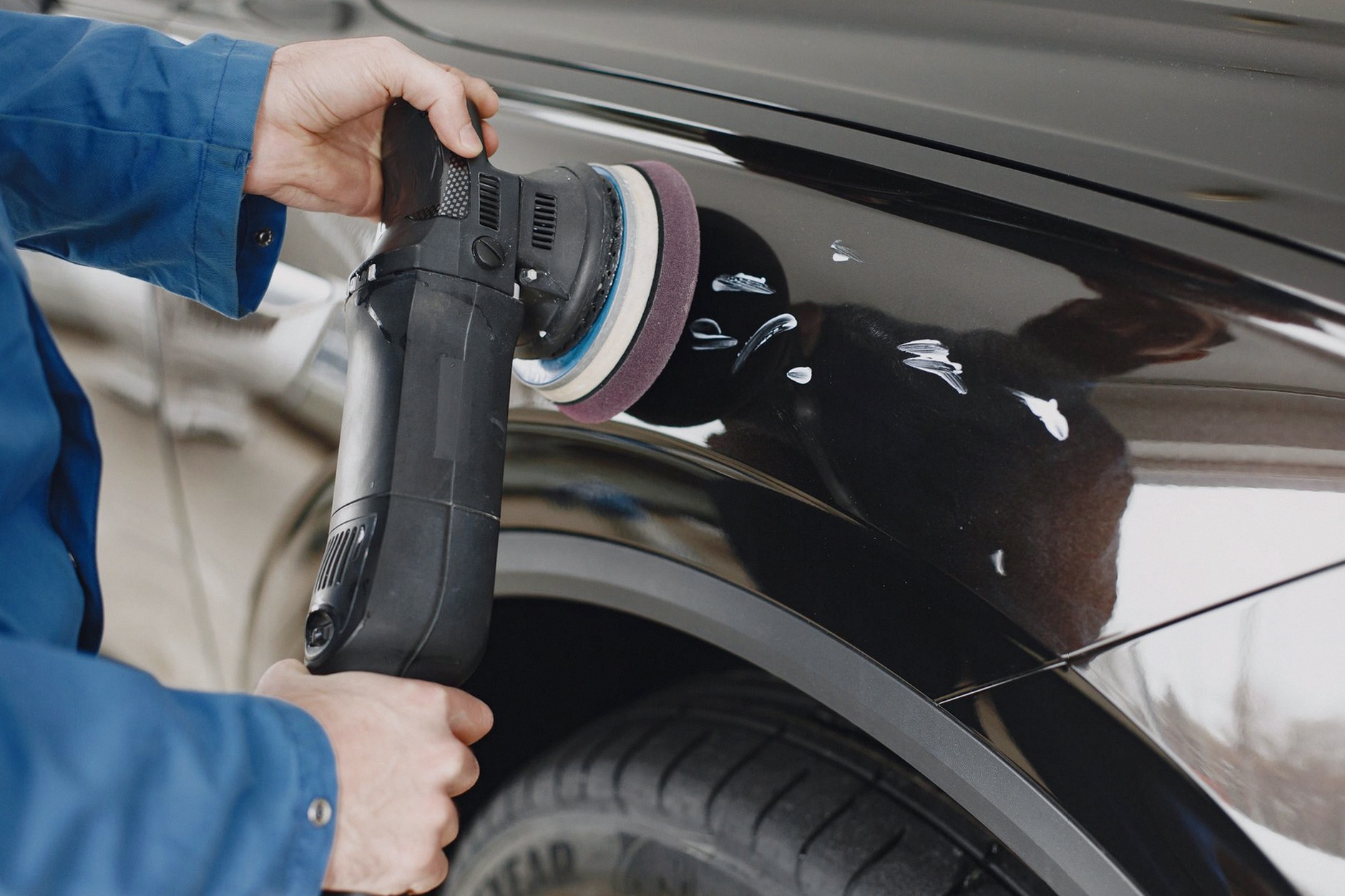 Hands using a polishing machine on a car's surface in a garage setting.
