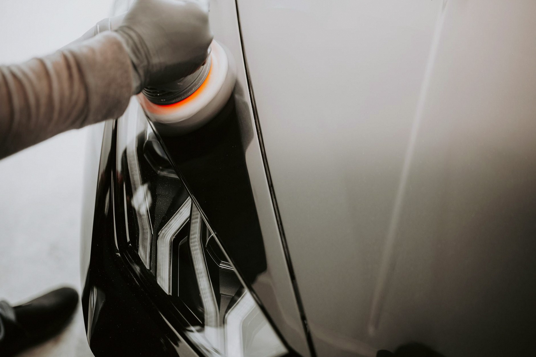 Close-up view of a person polishing a black car using a buffing machine.